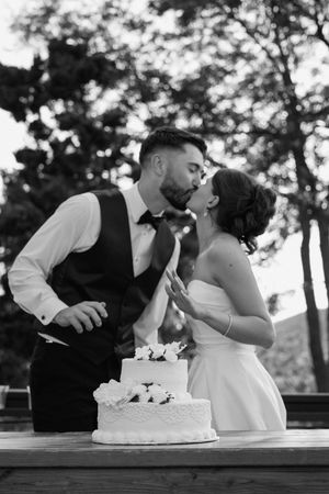 A couple shares a romantic moment with their wedding cake on an outdoor table.
