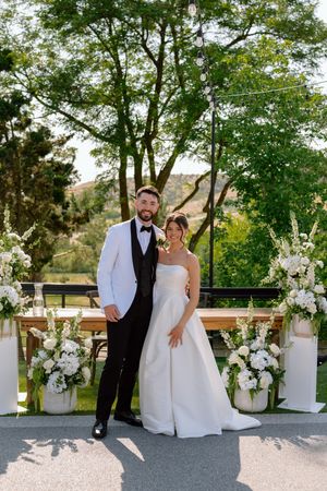 A wedding ceremony setup outdoors with white floral arrangements and natural greenery creating an elegant backdrop.