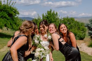 A group of people in formal attire share joyful moments together outdoors on a sunny day with green scenery.
