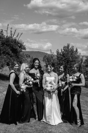 Wedding party in black dresses and white gown pose together outdoors in a series of candid moments.