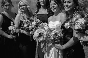 A black and white photo showing bridesmaids in dark dresses sharing laughter during a wedding celebration.
