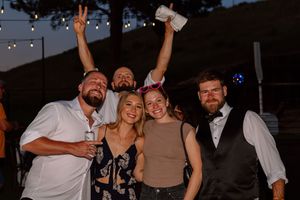 Group of friends celebrating at an outdoor party with drinks and peace signs in the evening.