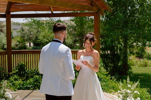 A couple exchanges vows during their outdoor wedding ceremony under a wooden pergola on a sunny summer day.