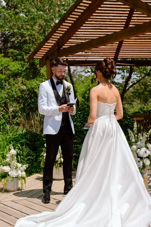 A couple shares a tender moment under a wooden pergola during their outdoor wedding ceremony.