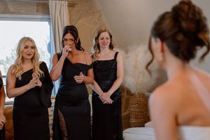 A group of bridesmaids in black dresses share an emotional moment with the bride during a wedding celebration.