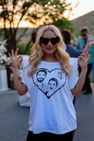 A person in a white t-shirt with a printed heart design makes peace signs while posing outdoors at sunset.
