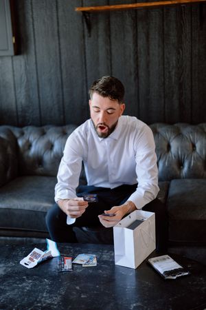 A person in a white shirt examines playing cards on a dark table in a moody, dramatic setting.