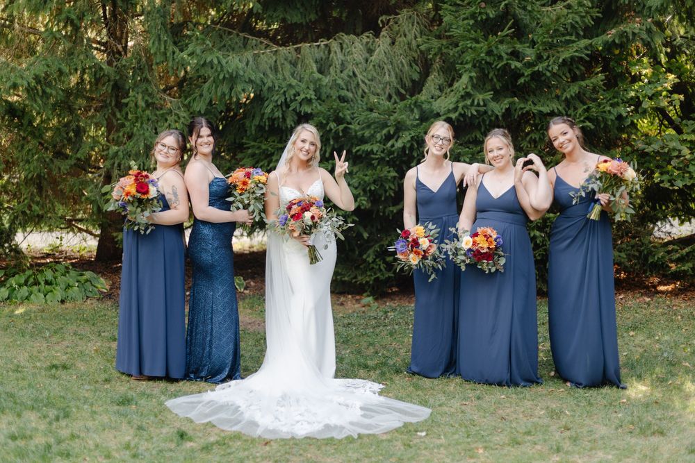 Wedding party in navy blue and white attire posing for group photos in garden setting.