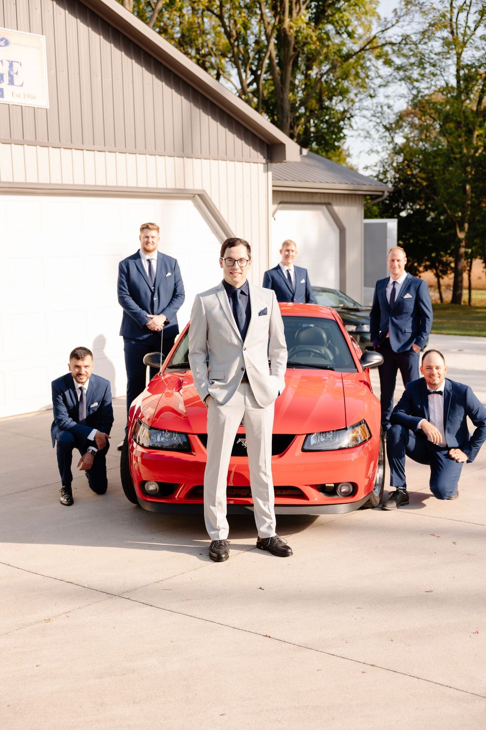 Groomsmen in suits pose playfully with a red sports car in a series of creative photos.