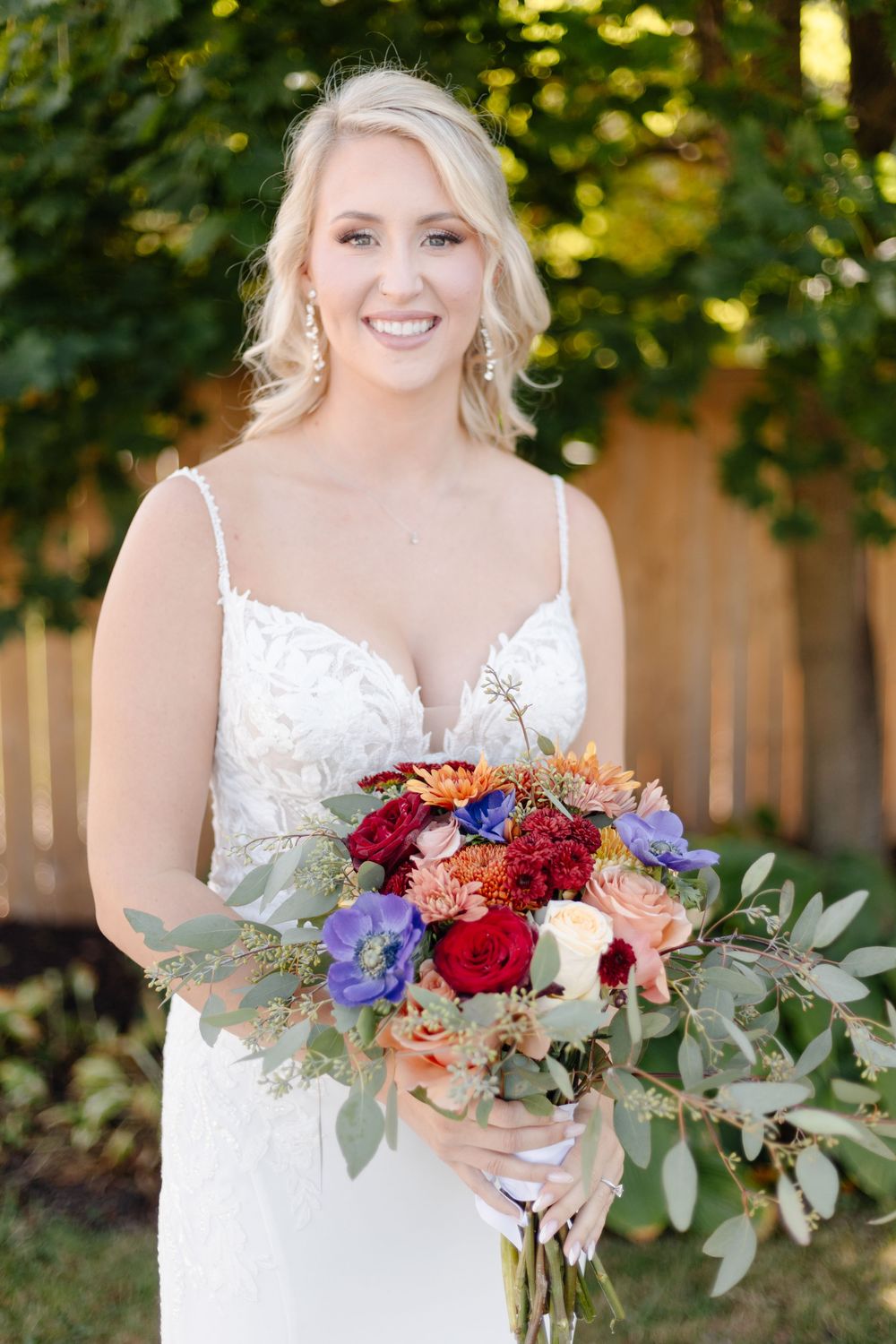 Beautiful bridal bouquet with red and orange flowers mixed with eucalyptus leaves against a sunlit garden backdrop.