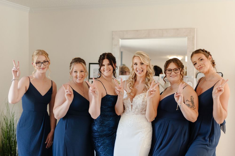 A group of women wearing coordinated navy blue and white outfits pose together with raised hands in celebration.
