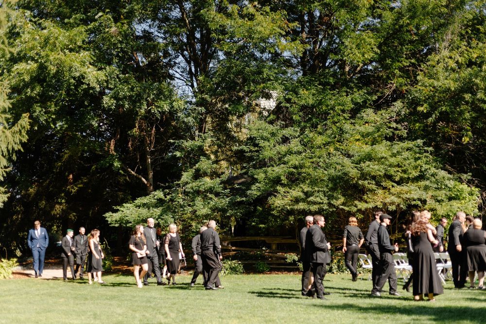 Wedding guests gather outdoors on a sunny day in a lush green park setting.
