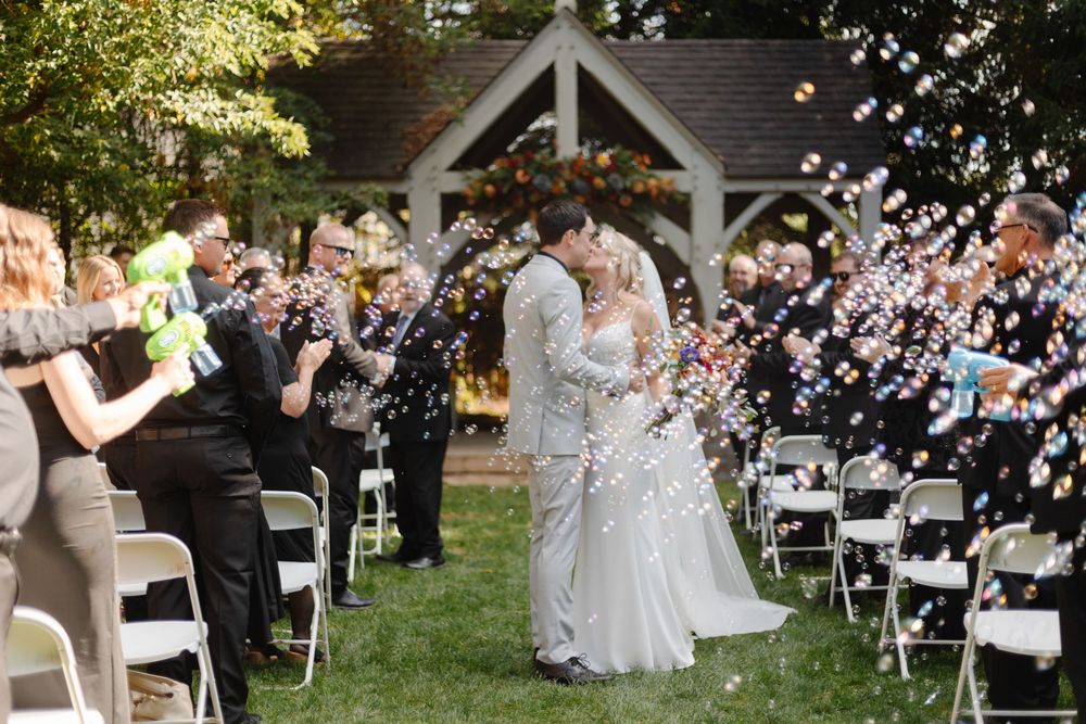Outdoor wedding ceremony setup with white chairs and floral arrangements under trees.