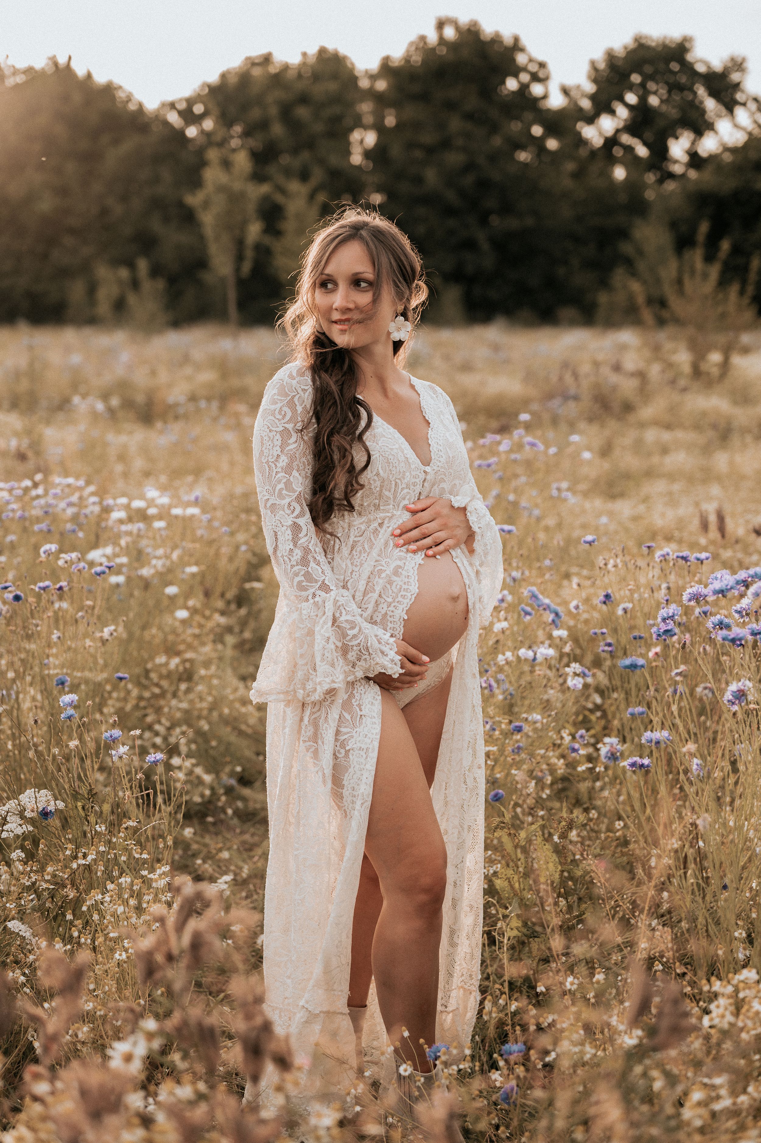 Dromerige zwangerschapsshoot in een wildbloemenveld bij zonsondergang, met fijne witte kanten robe — West-Vlaanderen: Roeselare, Ieper, Izeg