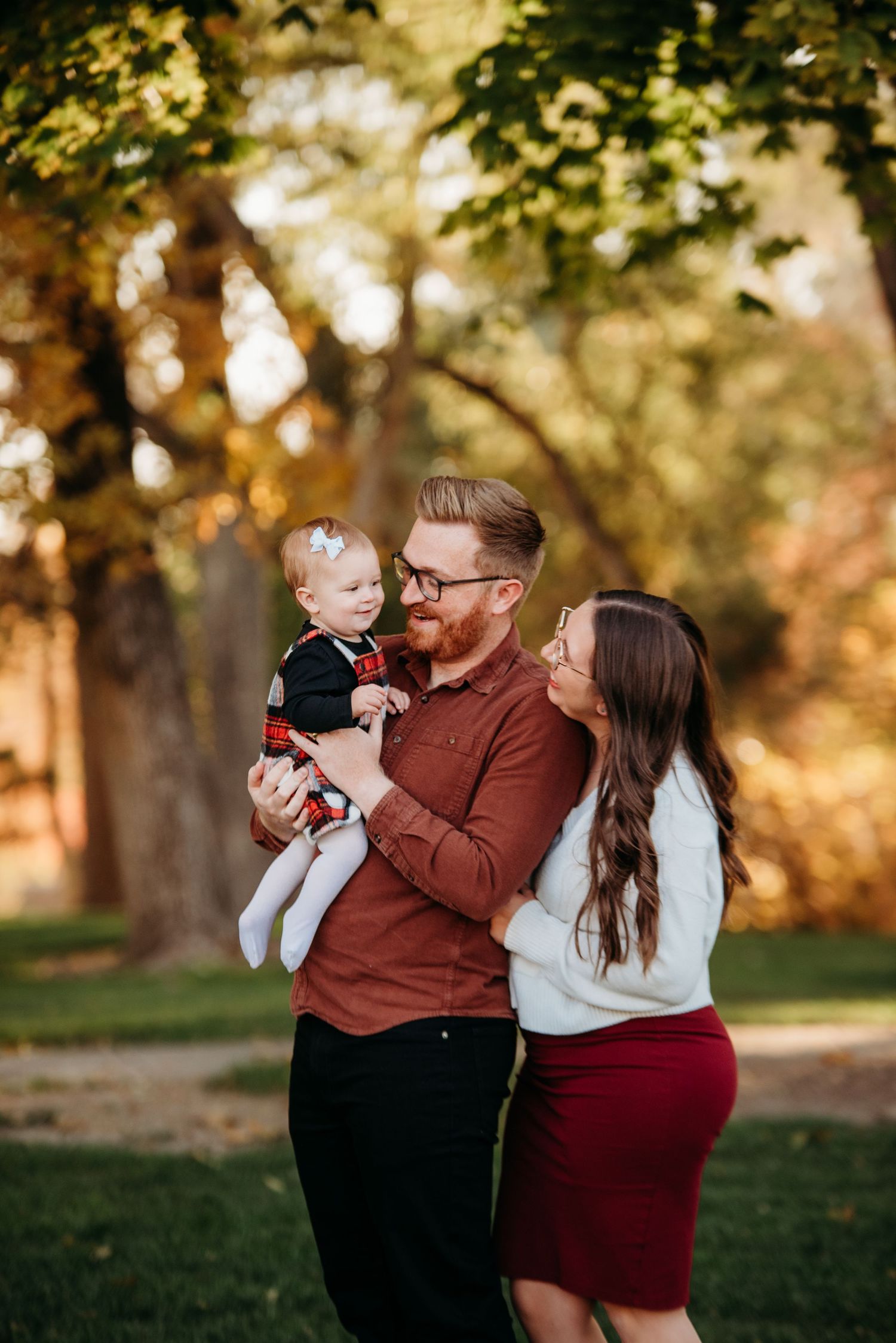 Family shares tender moments together in a park during golden hour with autumn trees in background.