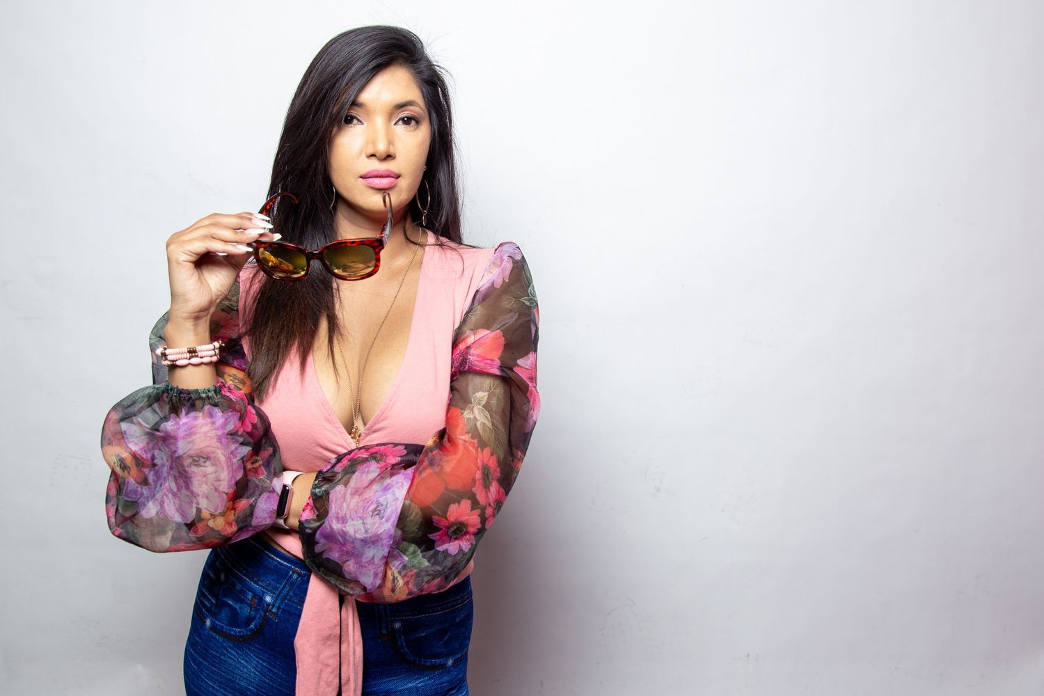 A woman in a sheer floral print blouse poses against a light gray background in a fashion photoshoot.