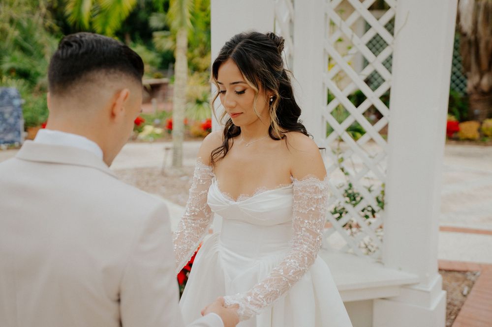 A romantic wedding moment under a white lattice gazebo with lace sleeves and an off-shoulder bridal gown.