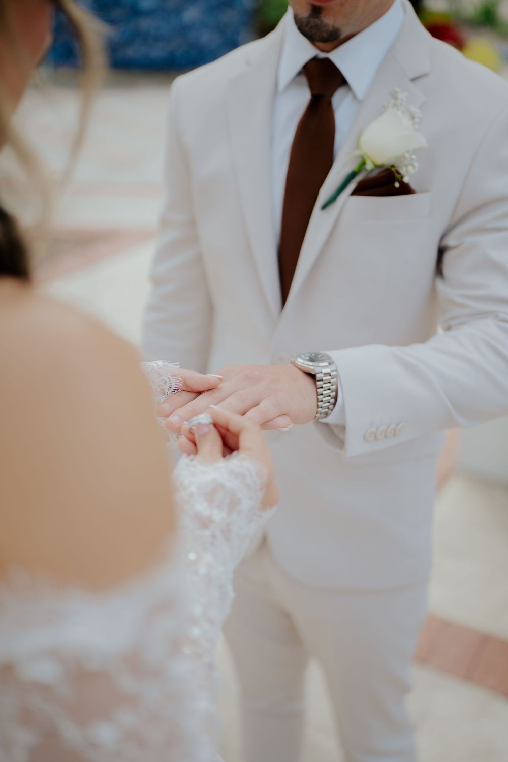 A series of wedding detail shots showing hands wearing a white suit jacket and brown tie.