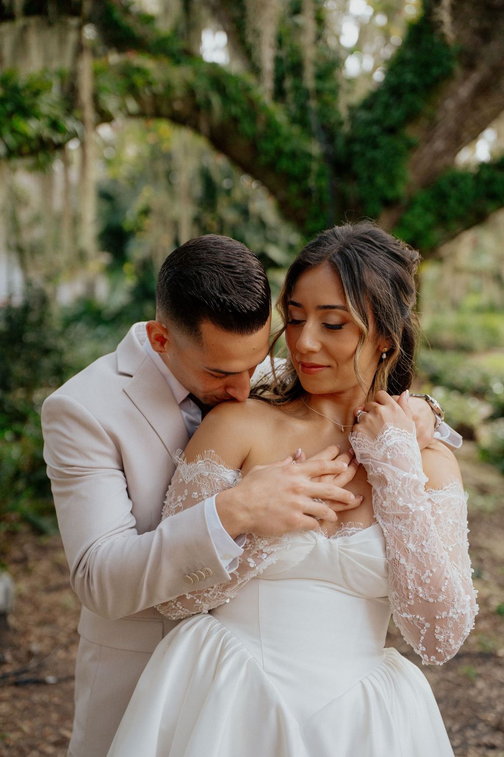A romantic wedding couple embraces in a garden setting with soft natural lighting.