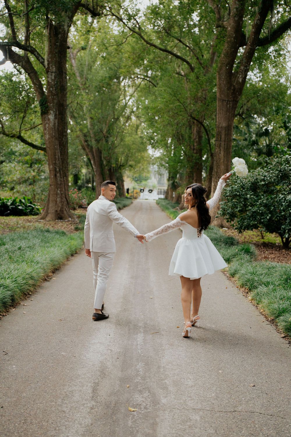 A playful couple holds hands and spins around on a tree-lined path during their photo session.