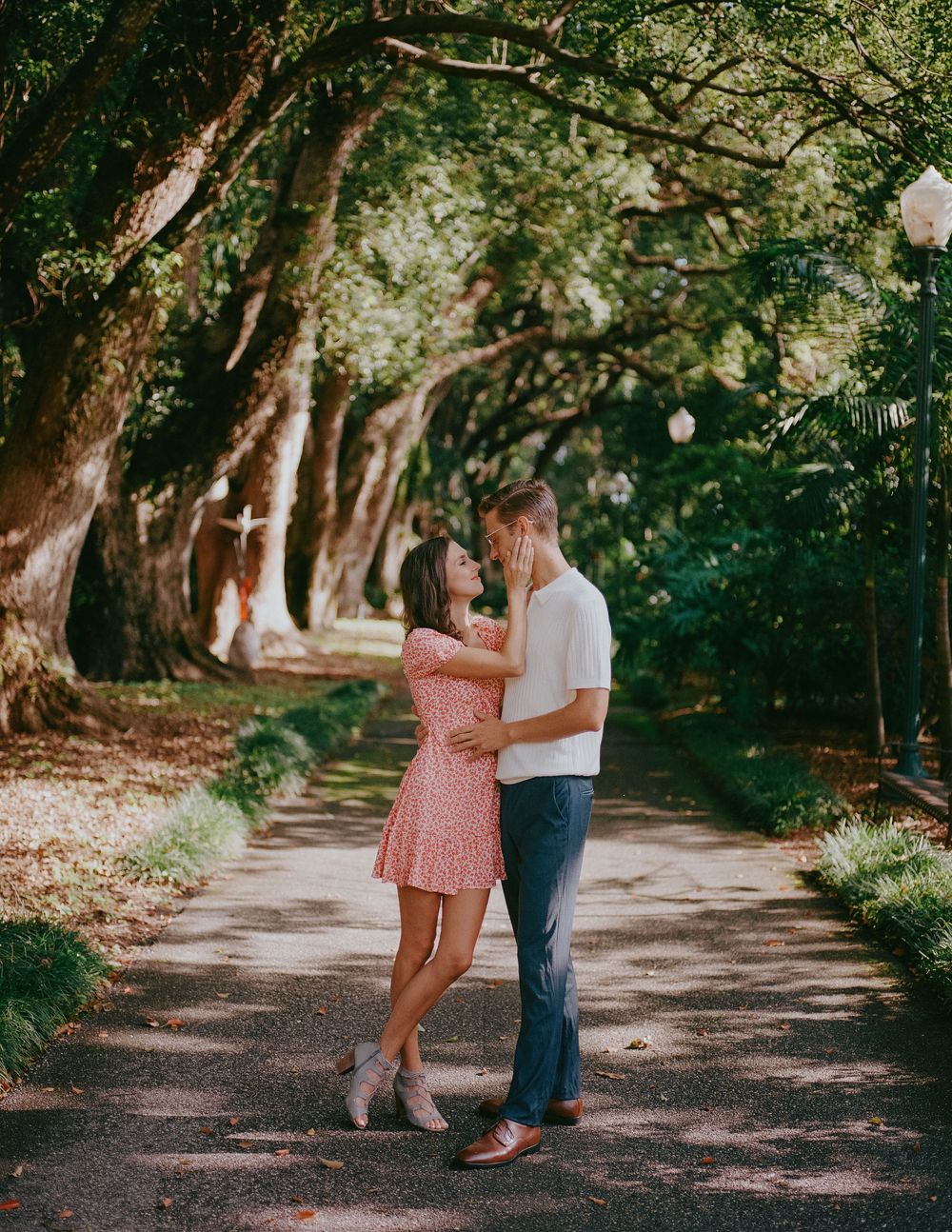 A couple shares a romantic moment on a tree-lined path during their engagement photoshoot.