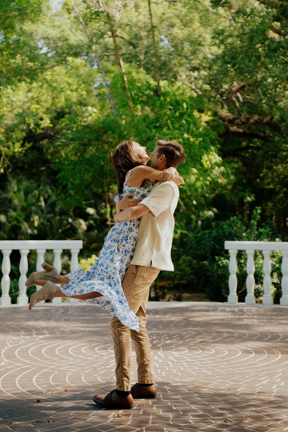 A couple dances together on a paved terrace surrounded by lush greenery and white balustrades.