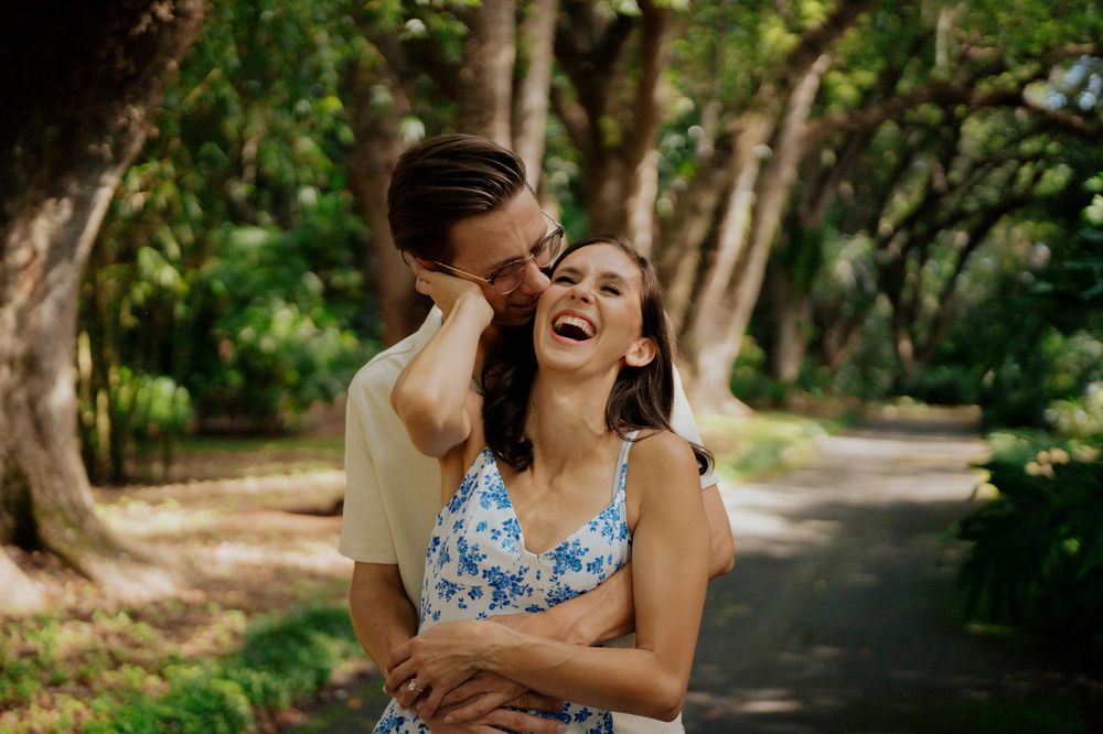 A couple shares joyful moments together on a tree-lined path in a lush green park setting.