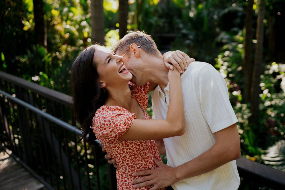 A couple in formal attire share a romantic dance pose in a sunlit outdoor garden setting.