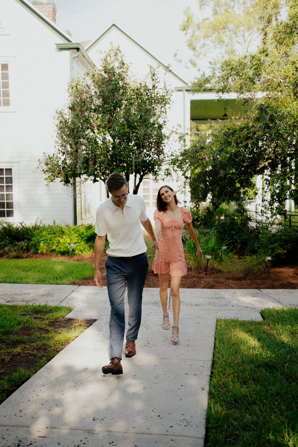 Two people walking together on a concrete path beside a white building and landscaped garden.