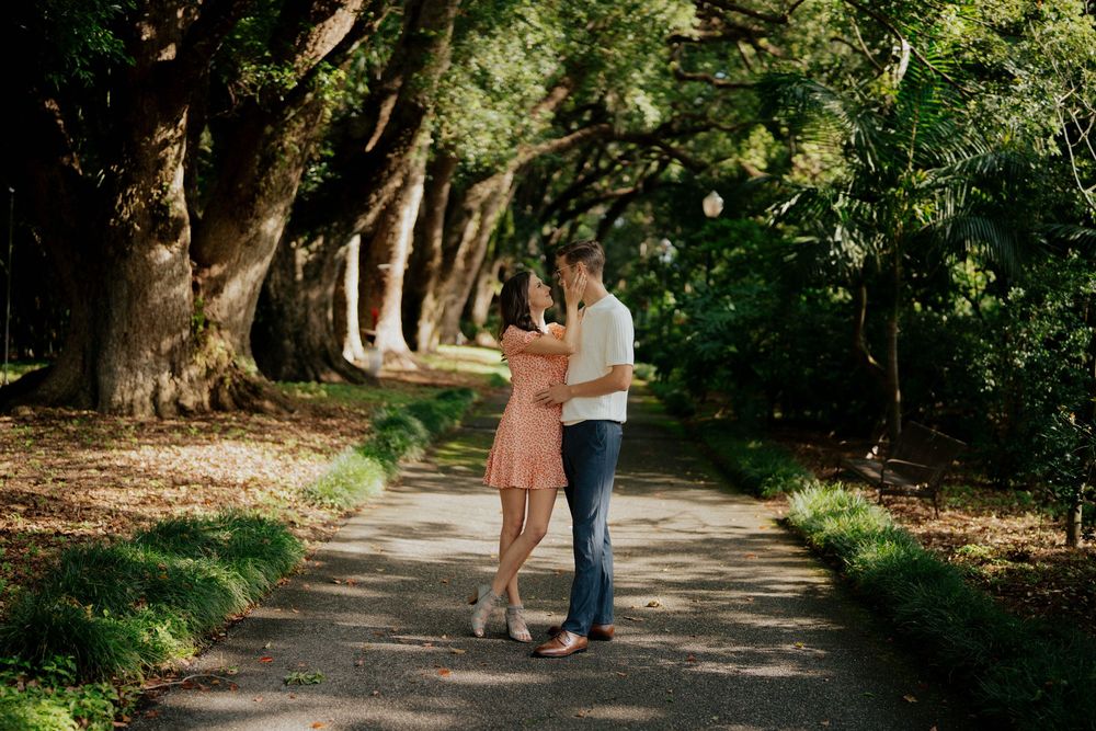 A couple walking hand in hand down a tree-lined path in a romantic outdoor setting.