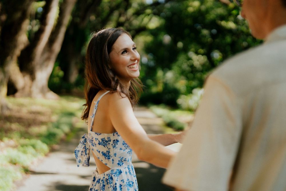 A couple shares a romantic moment in a garden setting wearing floral blue and white outfits.