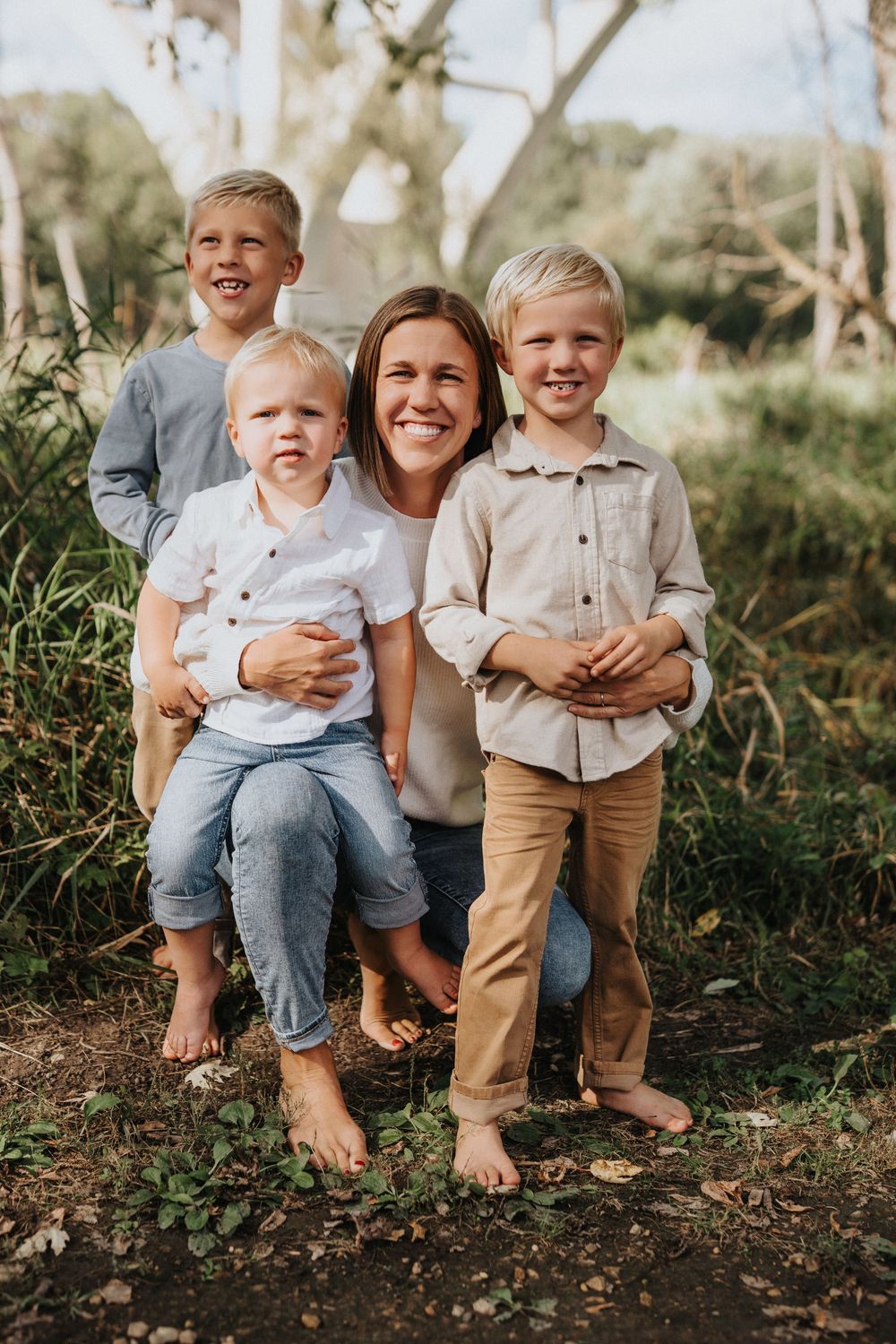 A candid outdoor family portrait featuring a parent and three children sitting together on natural ground.