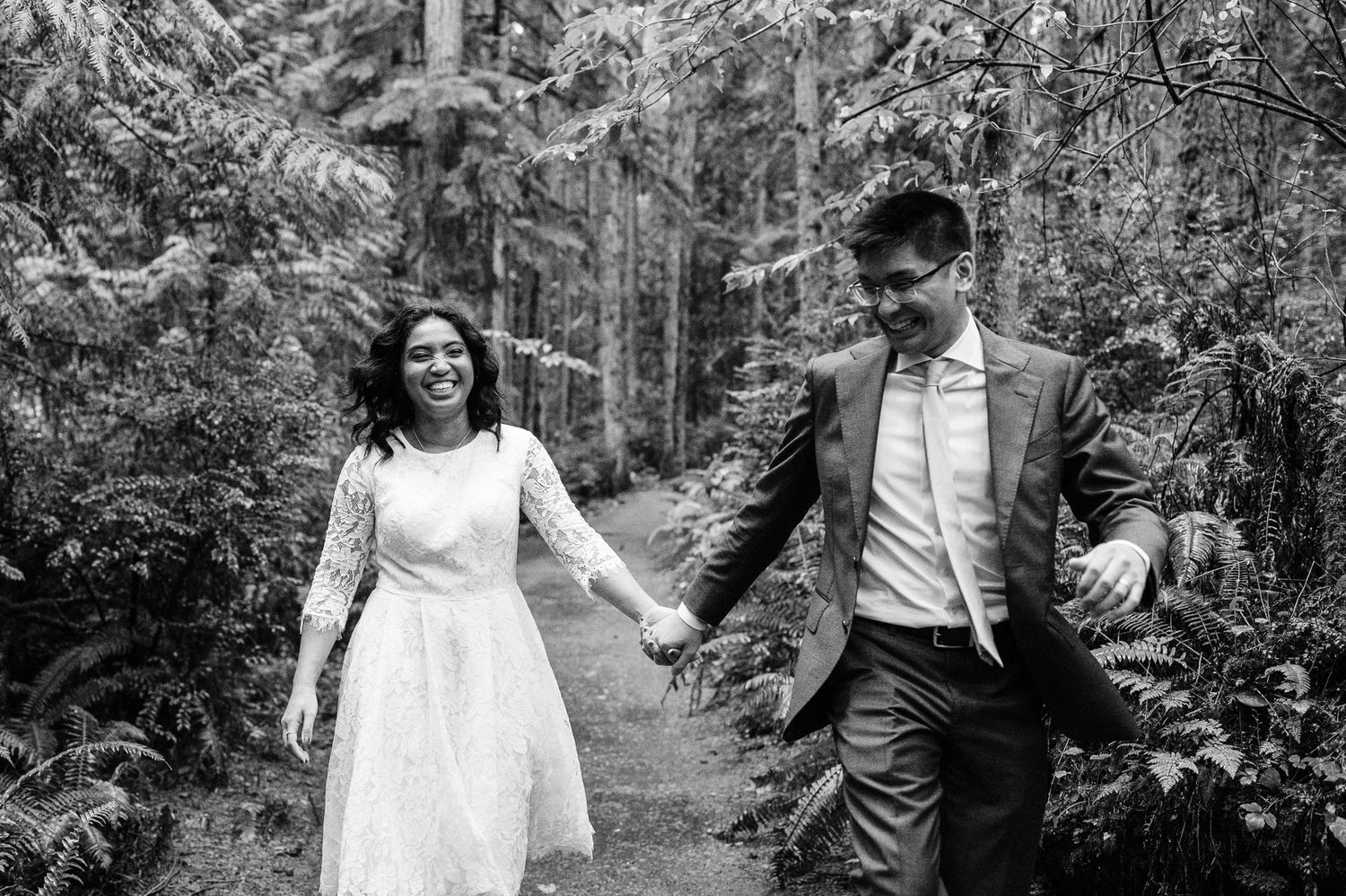 A couple in wedding attire walks through a lush forest setting during their outdoor photo session
