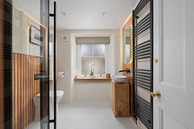 Modern minimalist bathroom with white walls, wood slat accents, and black metal details features clean architectural lines.