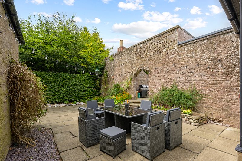 Outdoor patio area with gray wicker furniture and stone walls creating a cozy courtyard garden setting.