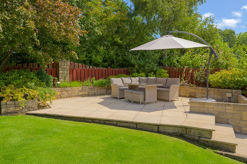 A modern backyard patio with stone steps, outdoor furniture, and lush green landscaping creates a tranquil outdoor living space.