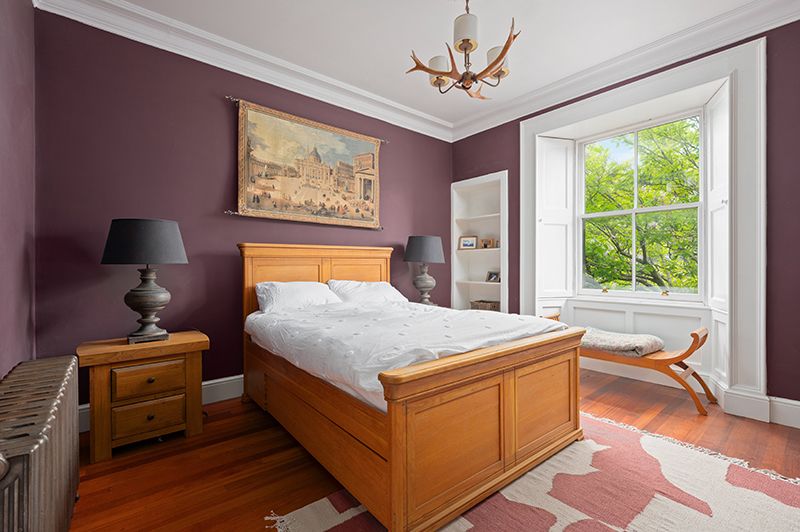 A cozy bedroom interior with wooden furniture, white walls, and natural light streaming through windows.