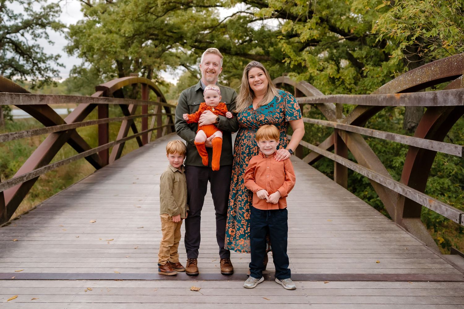 Family members pose together on a wooden bridge surrounded by autumn foliage.
