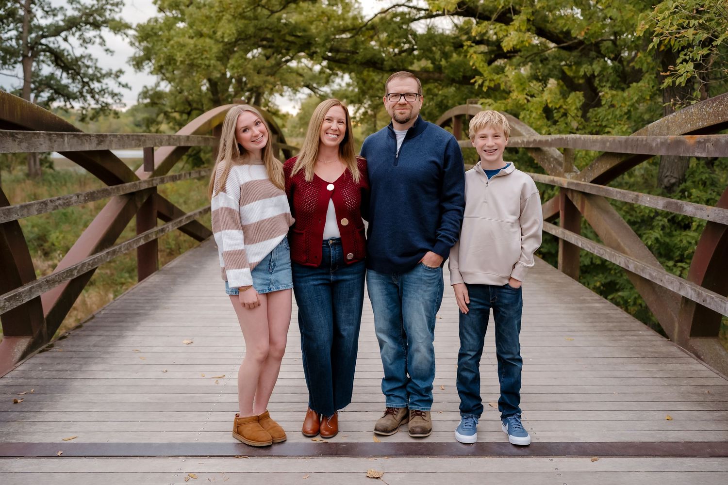 People arranged in casual poses on a rustic wooden bridge with natural greenery in the background.