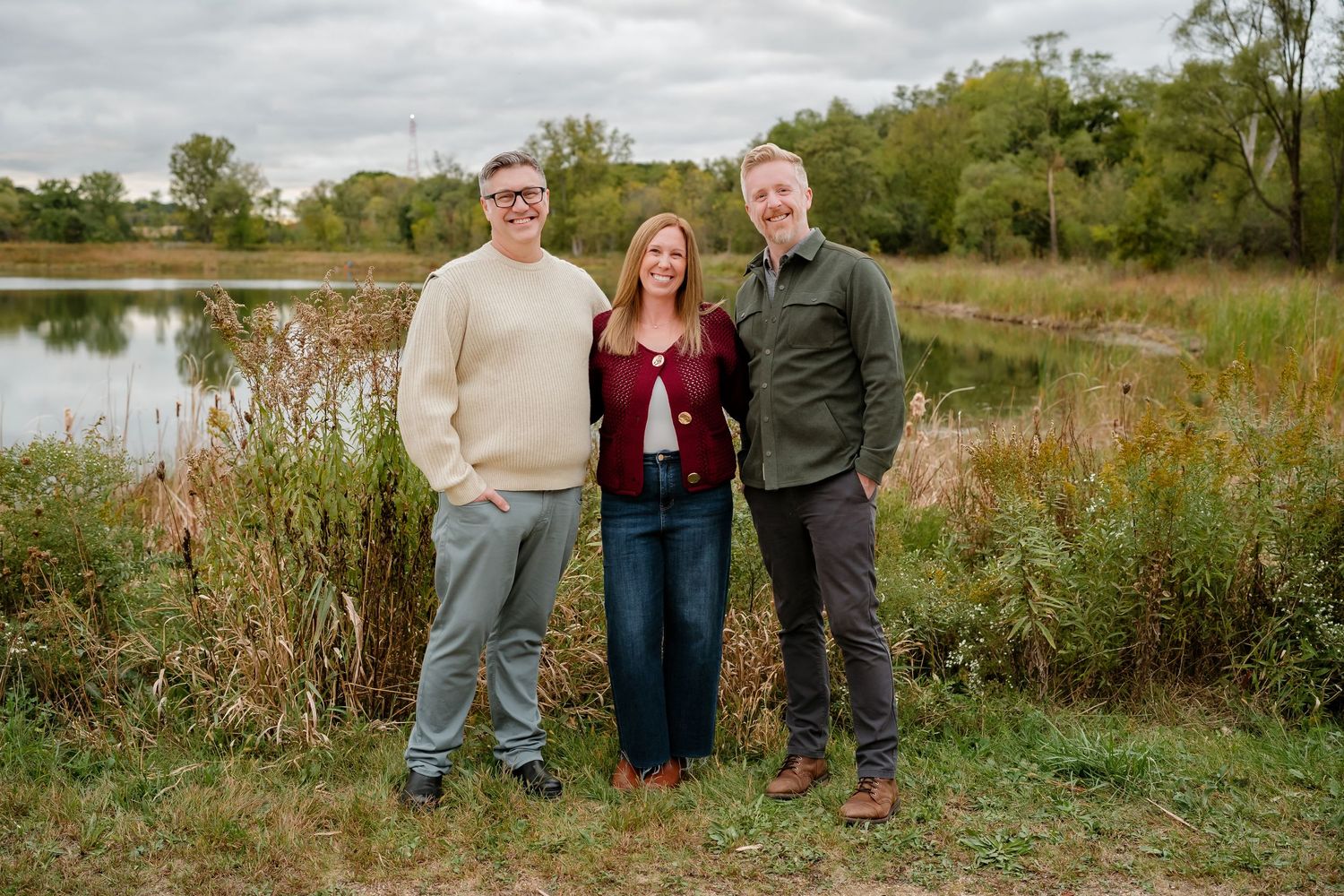 A group stands together in a natural outdoor setting with tall grass and trees during golden hour.