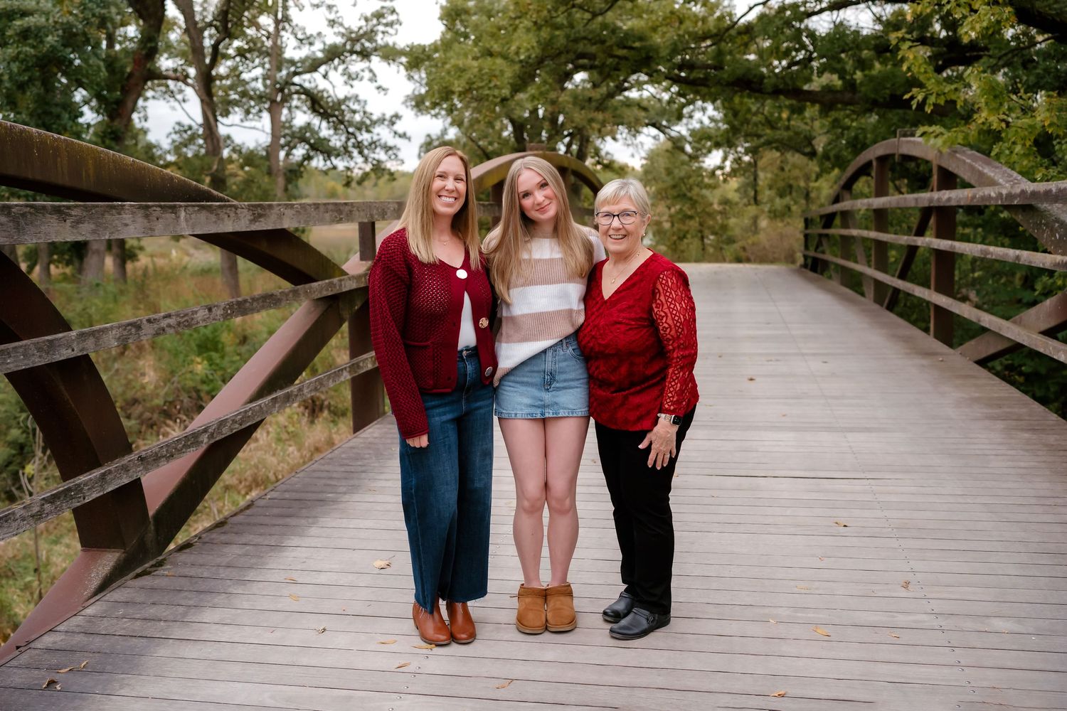 Three people stand together on a wooden bridge walkway in a park setting during autumn.