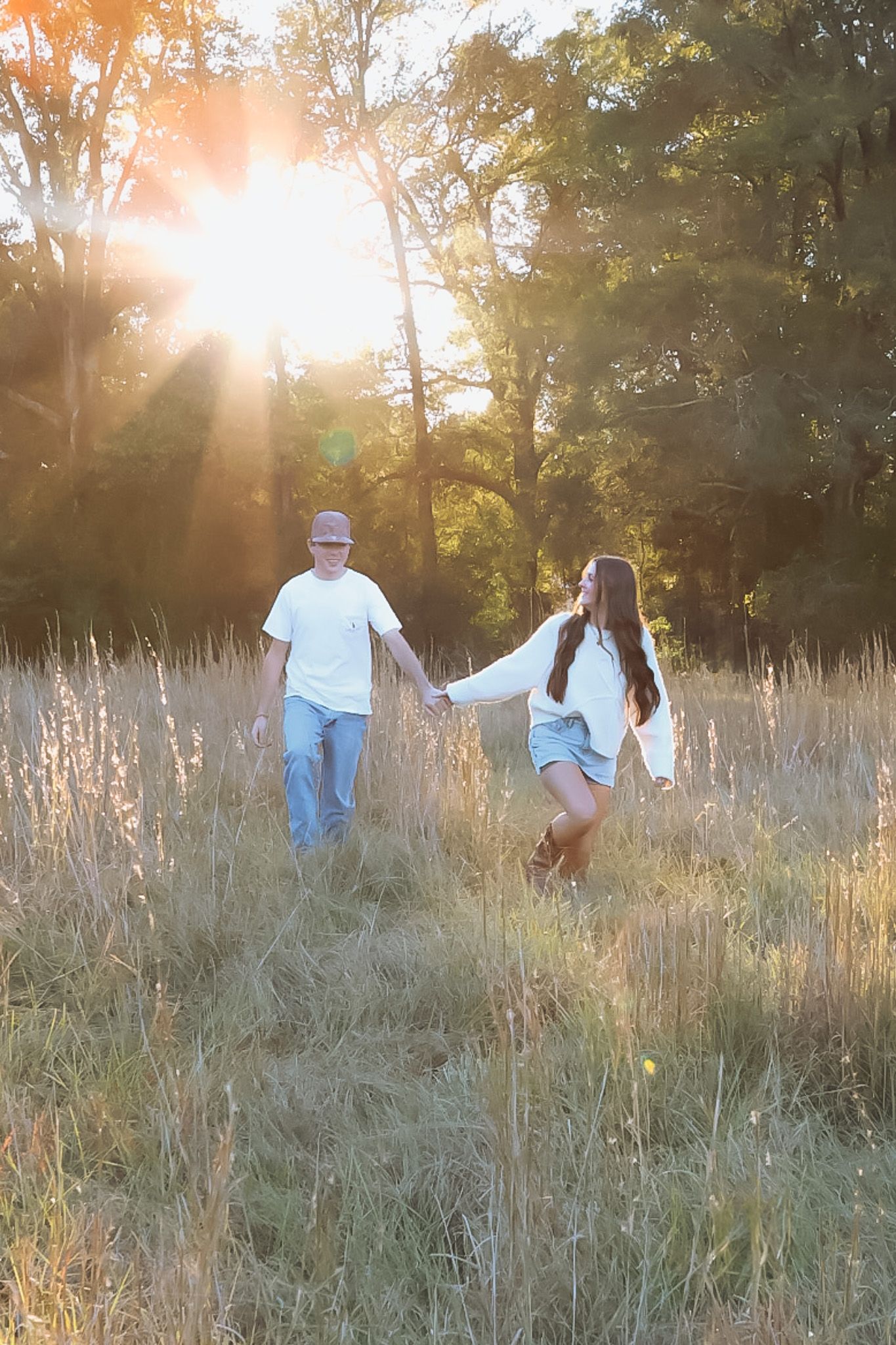Couple running through a sunlit field of tall grass at sunset.