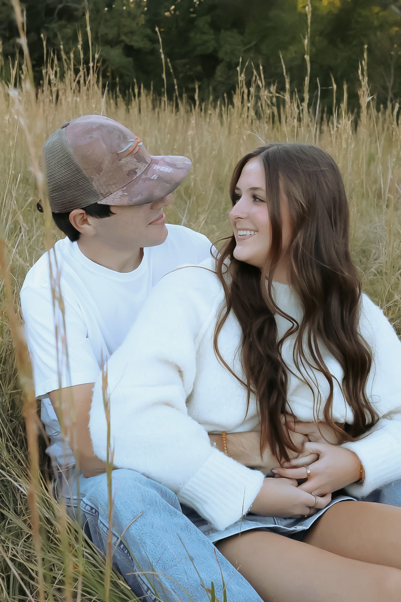 Couple in white shirts sitting together in a grassy field.