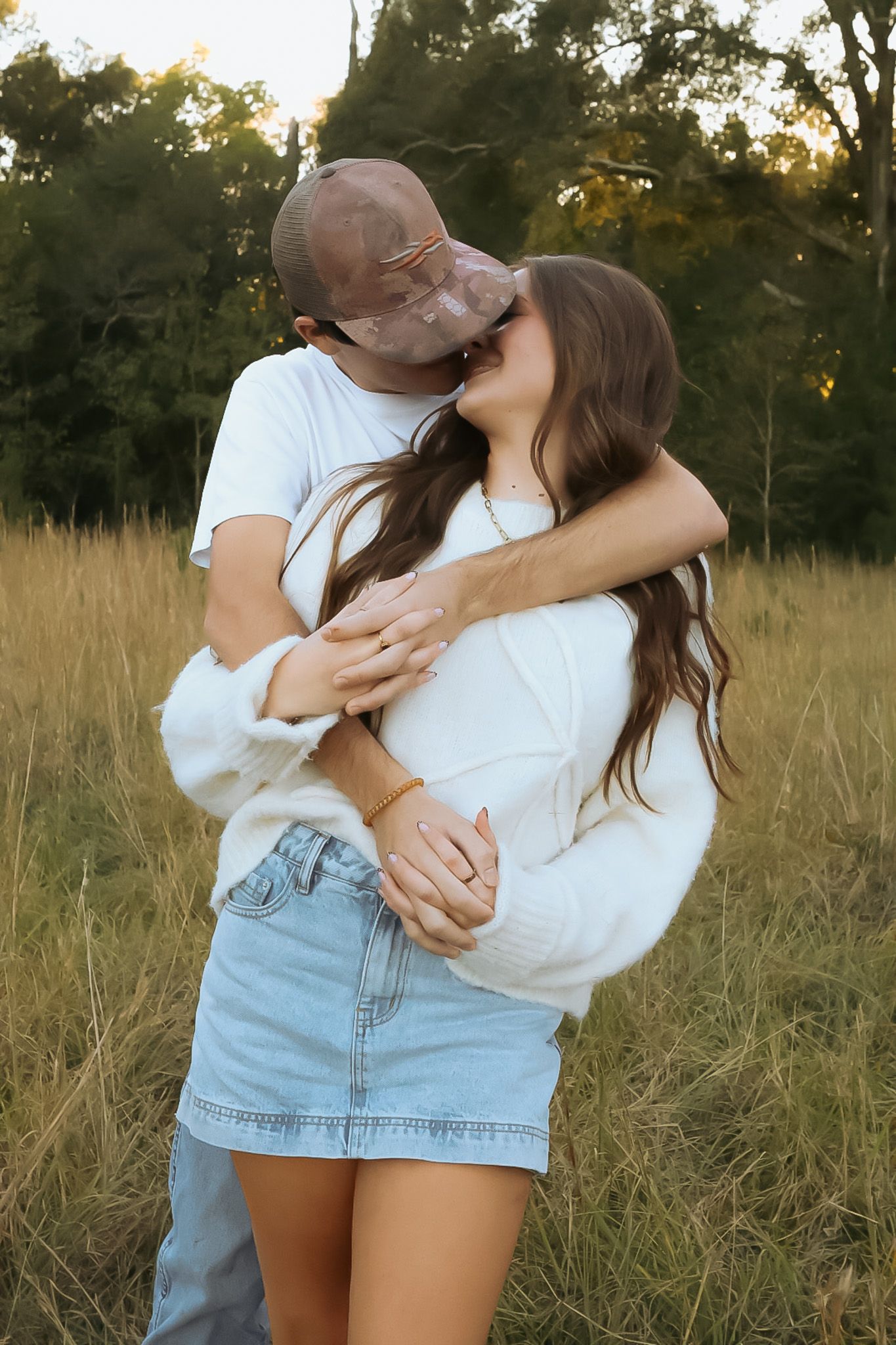 Couple in white shirts and denim embracing in a golden field at sunset.