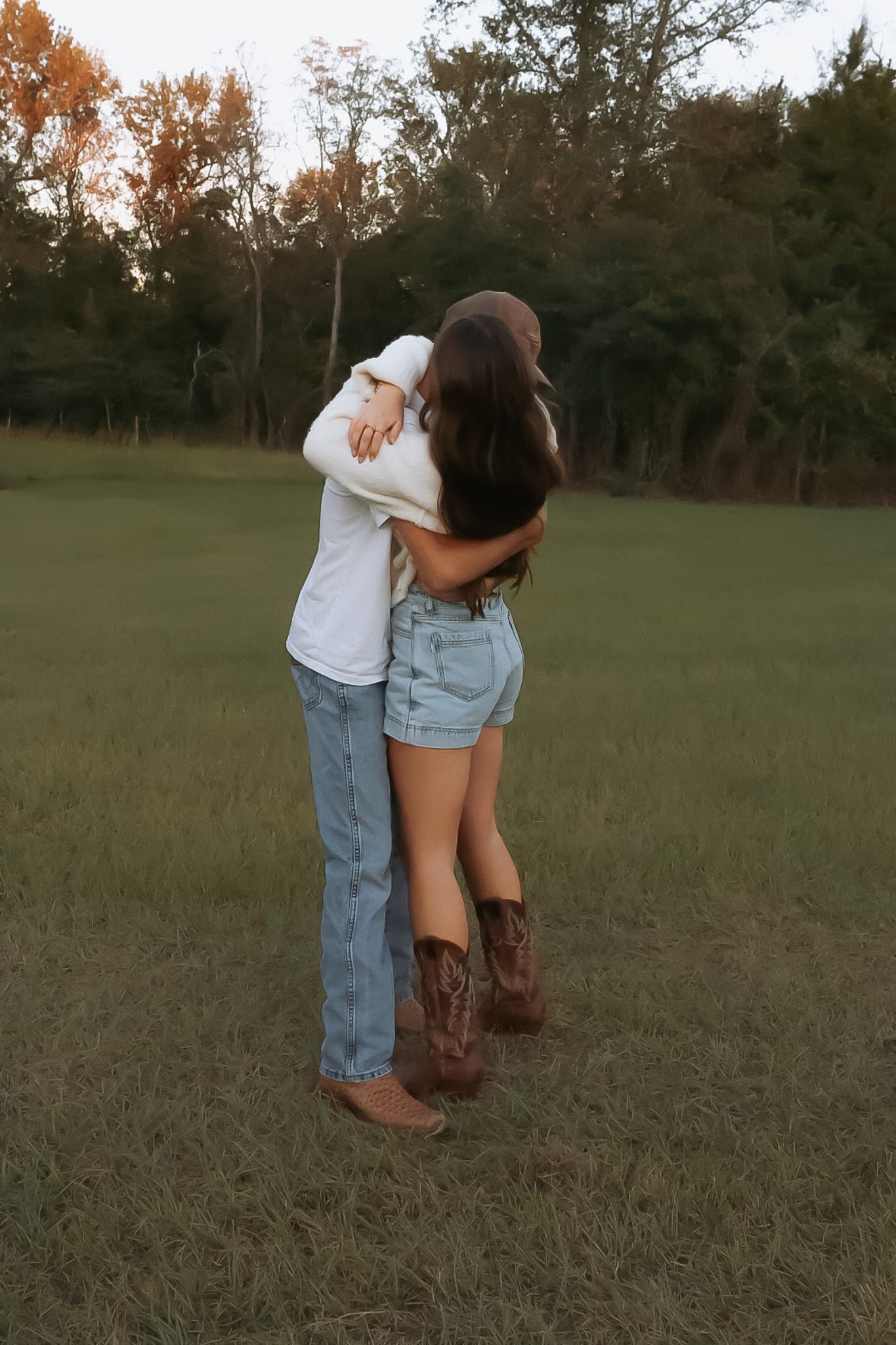 Couple in casual wear dancing together in a grassy field at sunset.