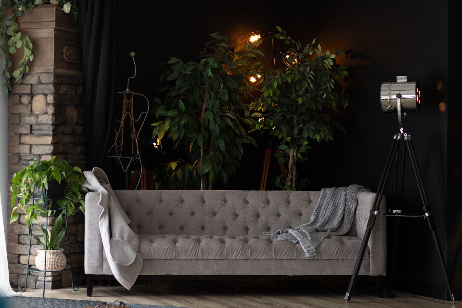 Modern lounge area with tufted gray sofas and lush greenery in an industrial-style space.