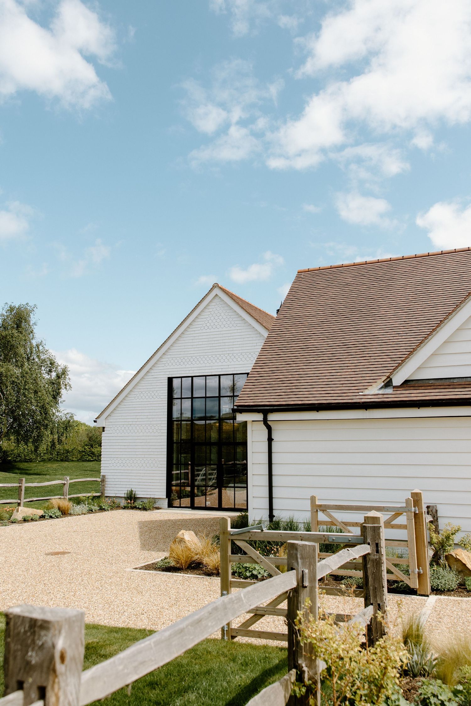 Modern white barn venue with black windows under blue sky and puffy clouds.
