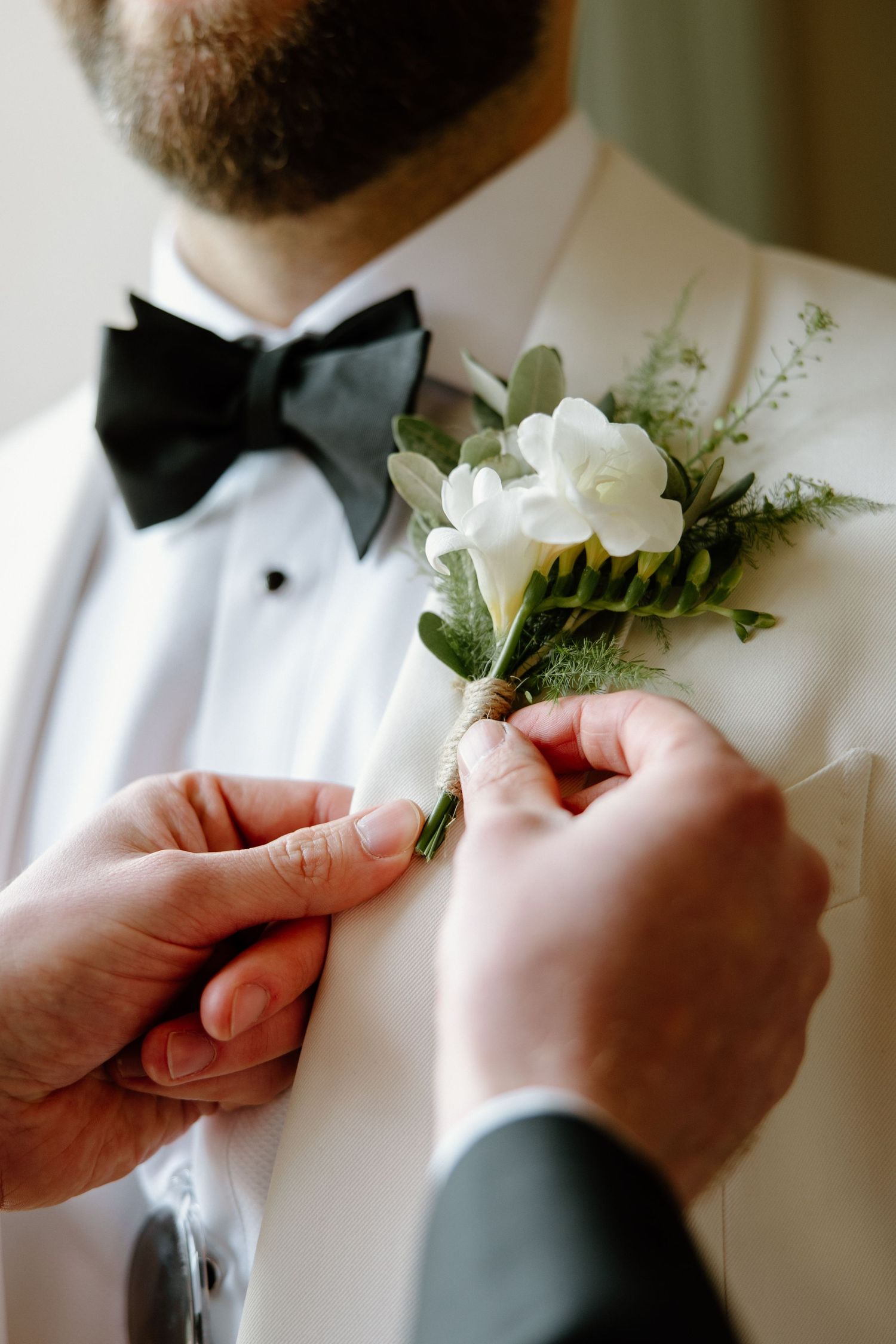 Close-up sequence of hands pinning white boutonniere flower to formal tuxedo lapel.