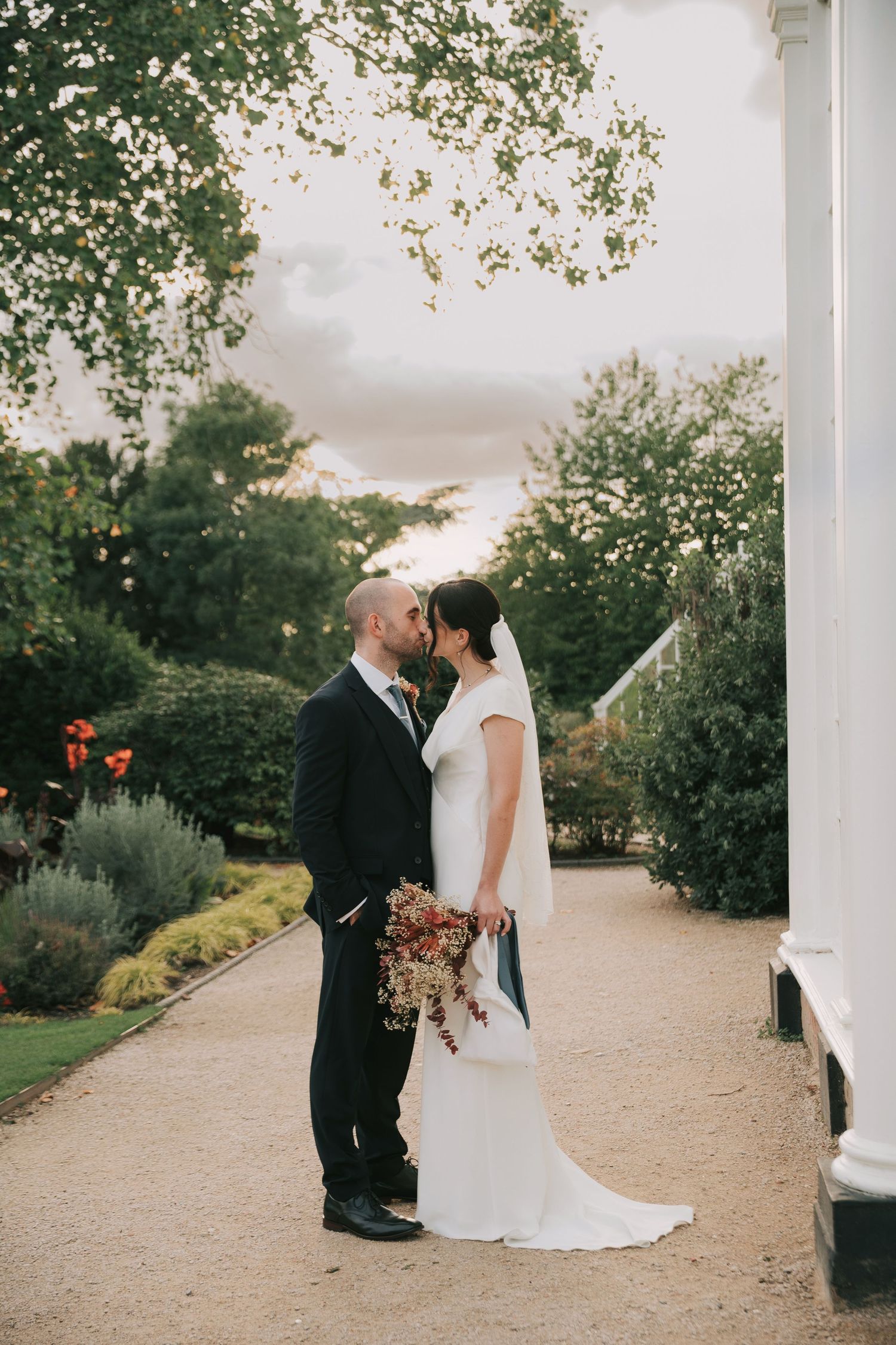 Romantic wedding couple sharing an intimate moment on a garden path surrounded by lush greenery.