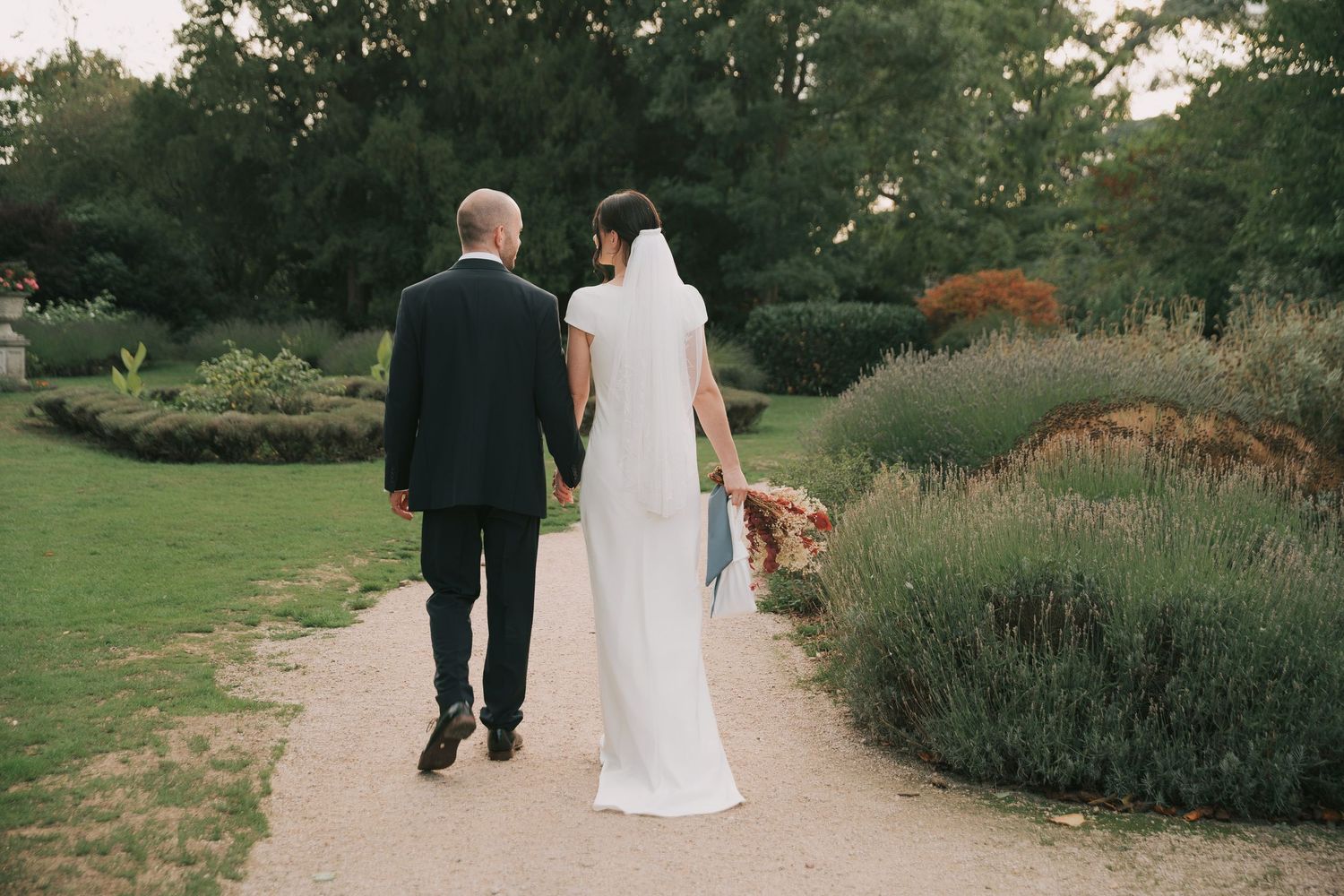 A couple walks together through a lush garden pathway during a wedding celebration.
